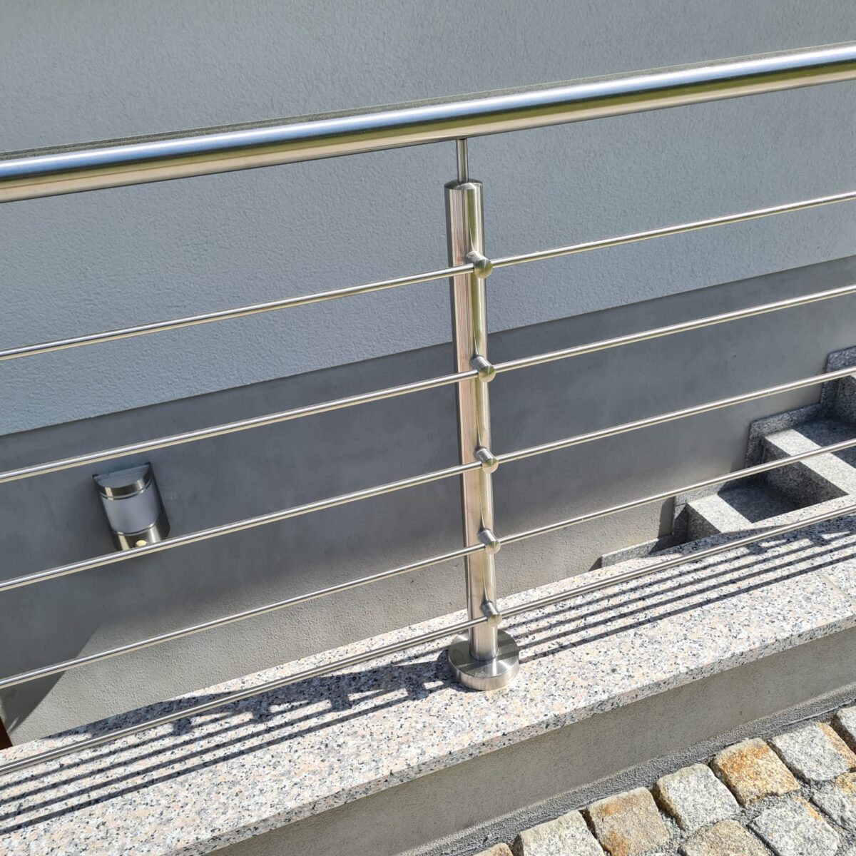 Edelstahl‑Außengeländer mit 5 waagerechten Füllstäben und gebogenem Handlauf an einer Kellertreppe.