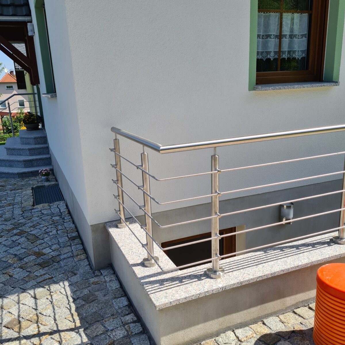 Edelstahl‑Außengeländer mit 5 waagerechten Füllstäben und gebogenem Handlauf an einer Kellertreppe.