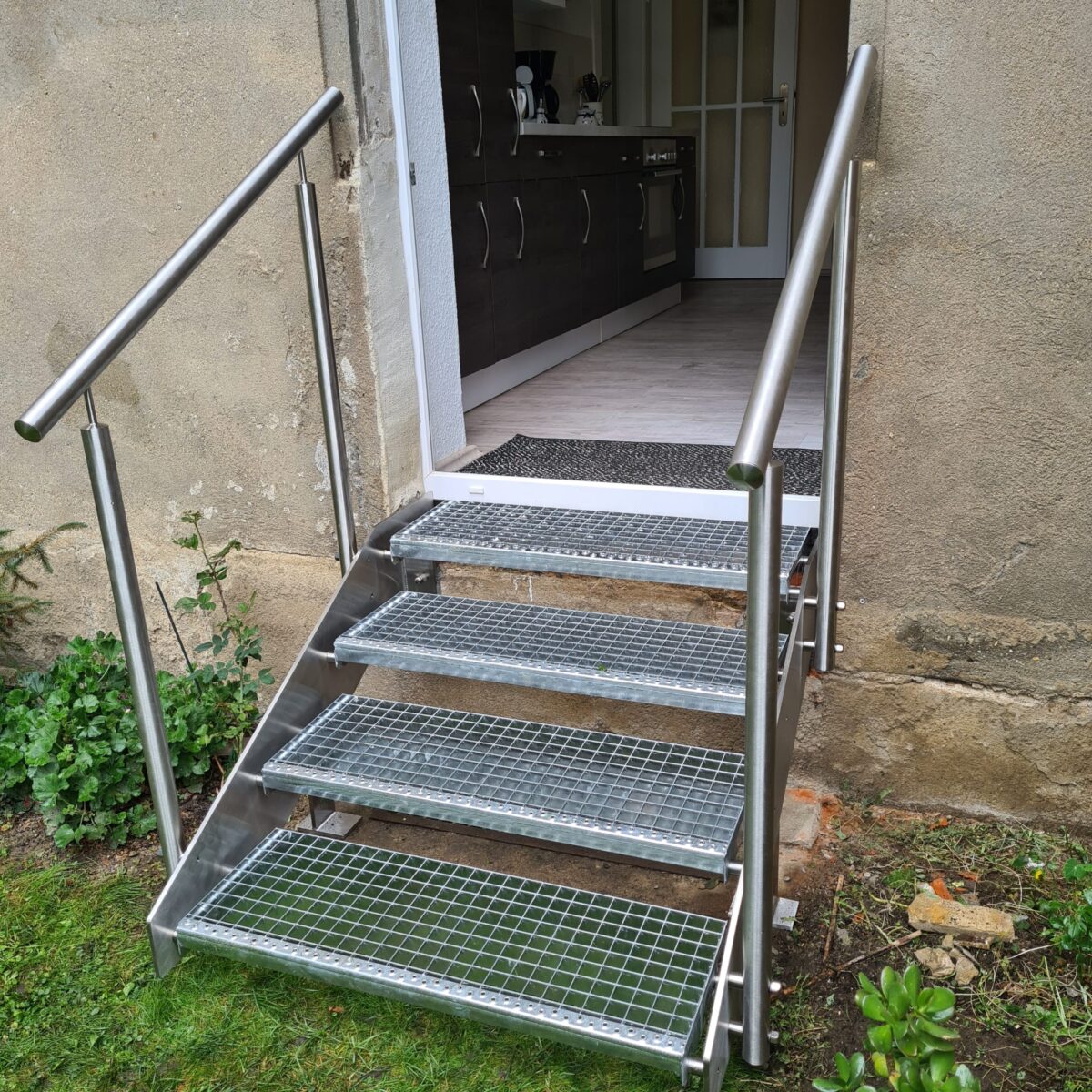 4‑stufige Edelstahl‑Gartentreppe mit Flachstahlwangen, Gitterroststufen und beidseitigem Handlauf.