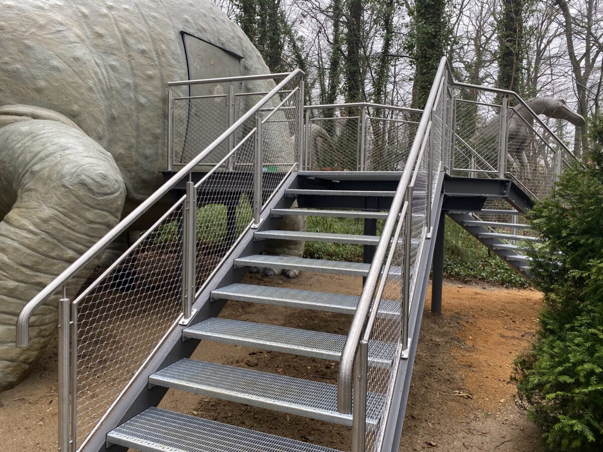 Zugangstreppe im Saurierpark mit pulverbeschichteten Stahlwangen und Edelstahlgeländer mit Seilnetzfüllung, gefertigt von Edelstahlverarbeitung Schmitt