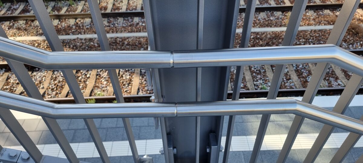 Doppelhandläufe aus Edelstahl mit gebogenen Endstücken und Befestigungsplatten an Bahnbrücken‑Stahlgeländer – gefertigt von Edelstahlverarbeitung Schmitt.