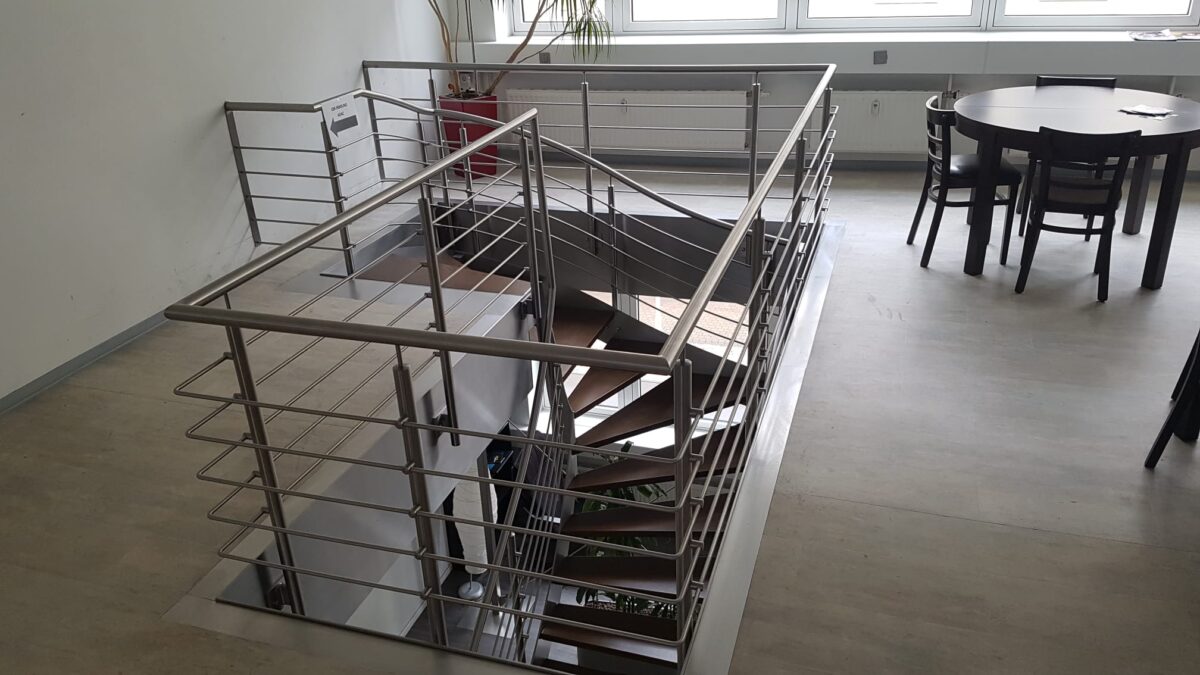Halbgewendelte Edelstahlwangentreppe mit Holzstufen und Füllstabgeländer – gefertigt von Edelstahlverarbeitung Schmitt aus Sohland/Spree für ein Geschäftsgebäude in Leipzig.