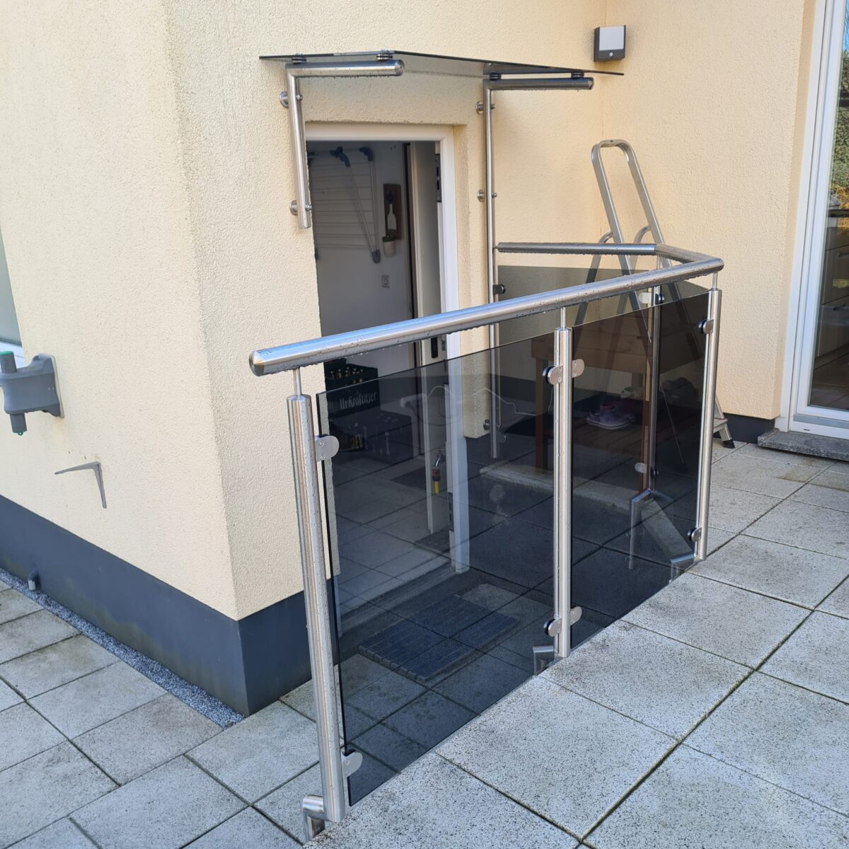 Vordach aus Edelstahl mit punktgehaltenem, grau getöntem Glas und passendem Edelstahlgeländer – gefertigt von Edelstahlverarbeitung Schmitt aus Sohland/Spree für ein Wohnobjekt in Radebeul.